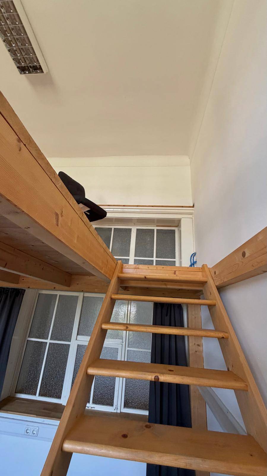 Holzleiter führt zur oberen Empore, mit Blick auf ein Fenster mit Sprossen im Hintergrund.