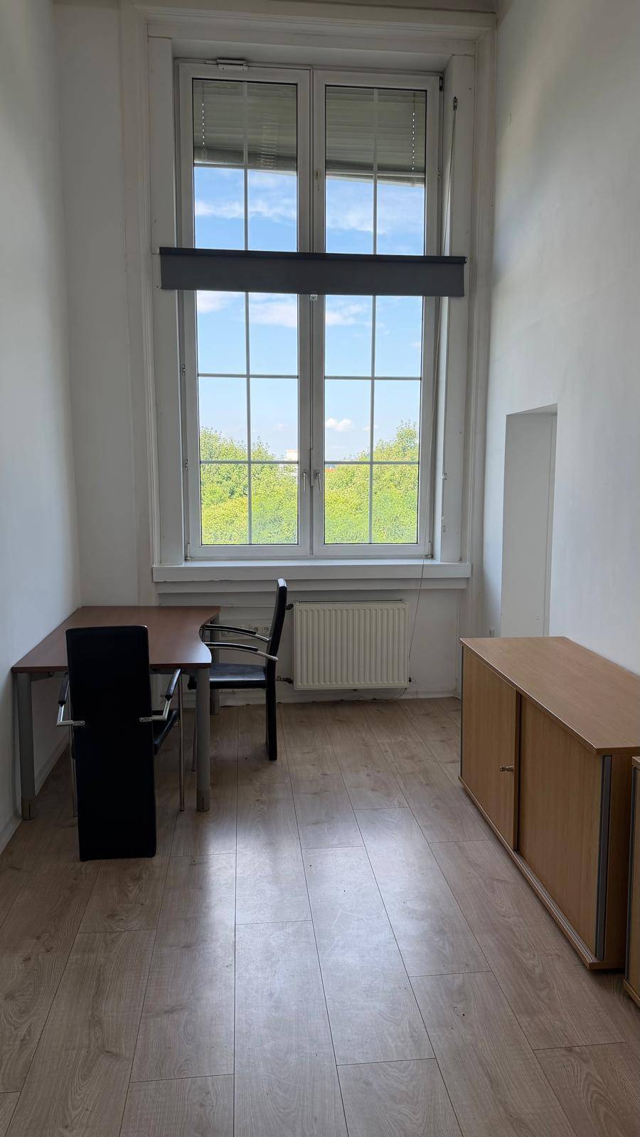 Büro mit hellem Laminatboden, einem Schreibtisch und einem großen Fenster mit Blick ins Grüne, ideal für konzentriertes Arbeiten.