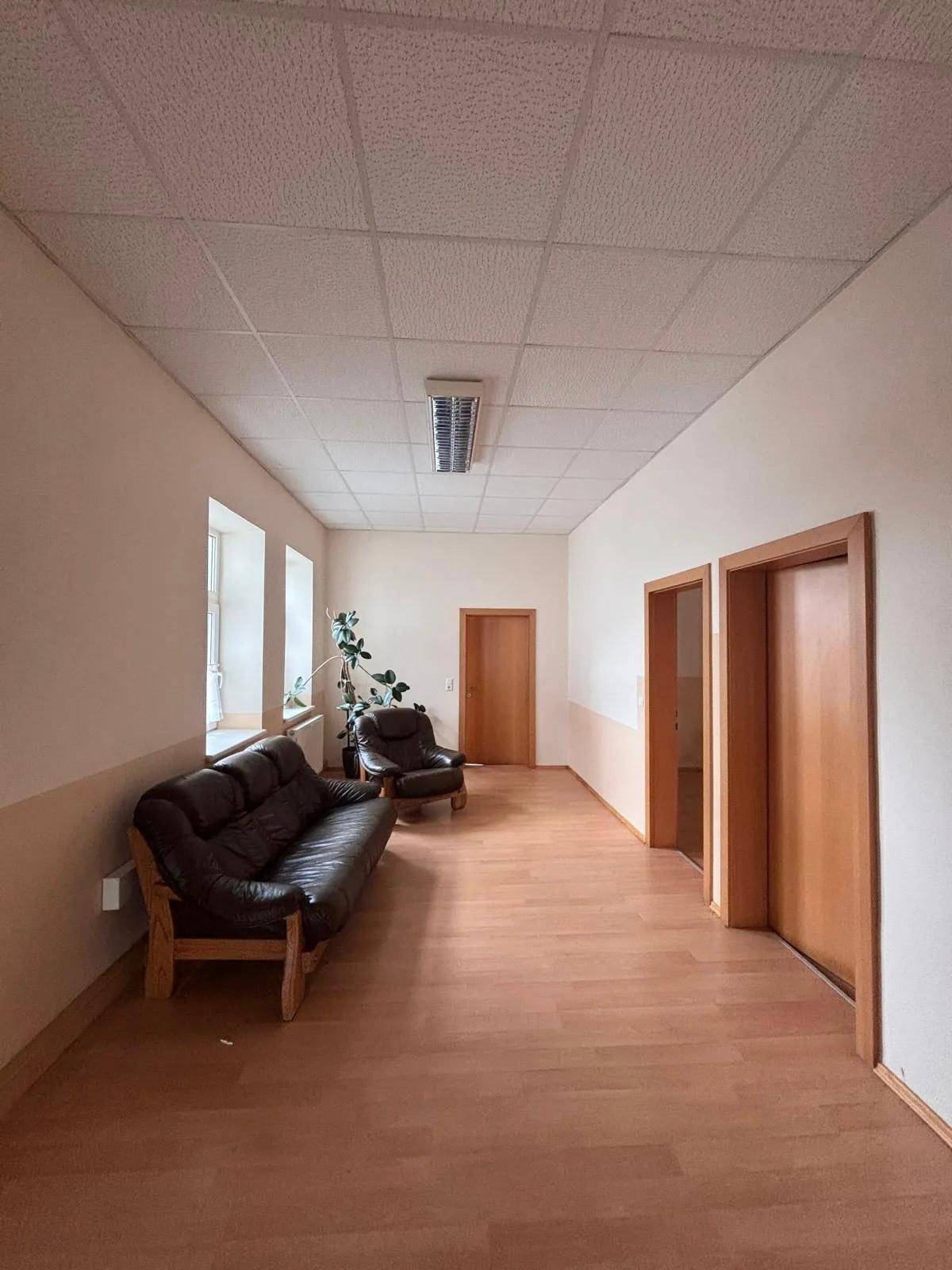 Heller Flur mit Holzboden, beigen Wänden und einer gemütlichen Sitzecke mit Ledersofa und Sessel.