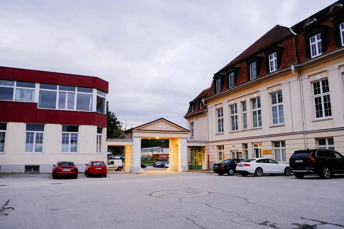 Eingangsbereich des Gebäudes mit einem Torbogen und einem großen Parkplatz, umgeben von Gebäudeteilen.