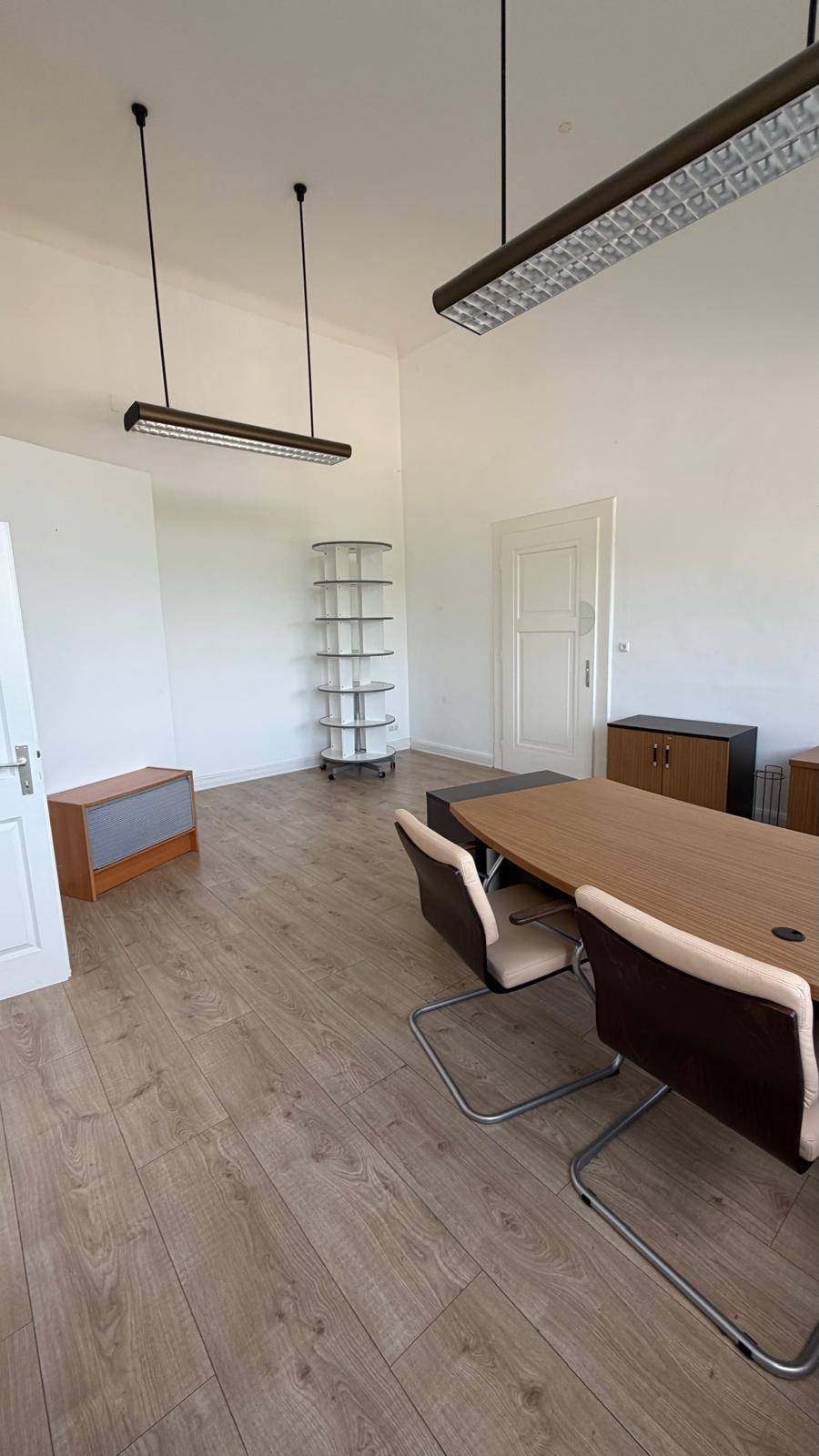 Geräumiges Büro mit hellem Laminatboden, weißen Wänden und modernen Hängelampen.