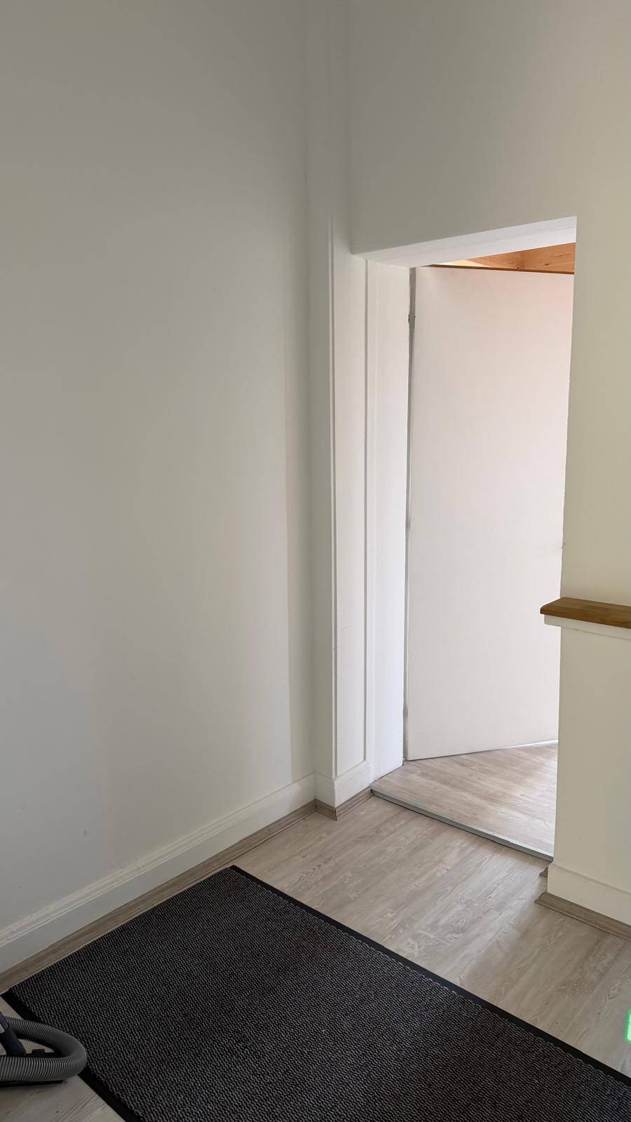 Schlichter Flur mit hellem Laminatboden und einer weißen Tür, die in einen weiteren Raum führt.