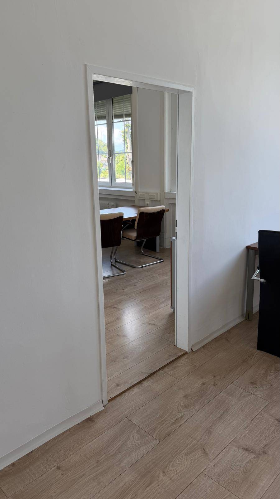 Türöffnung zu einem hellen Büro mit Laminatboden und Büromöbeln, von einem anderen Raum aus gesehen, schafft eine offene Verbindung.