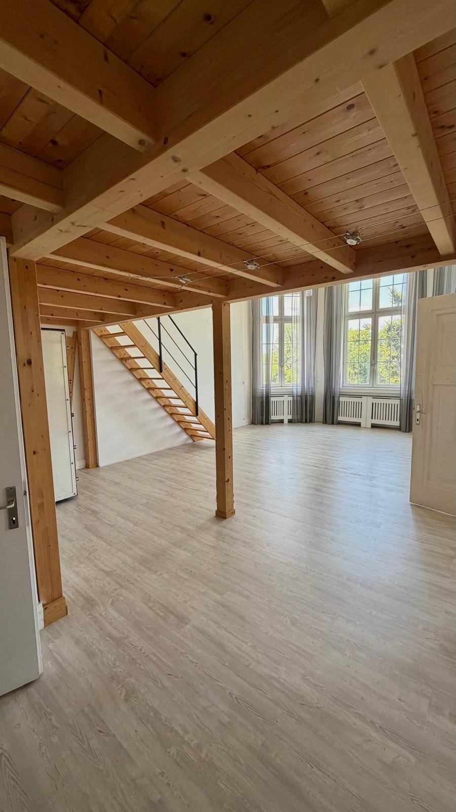 Geräumiger Wohnbereich mit sichtbaren Holzdeckenbalken und einer Treppe, die in eine obere Etage führt.