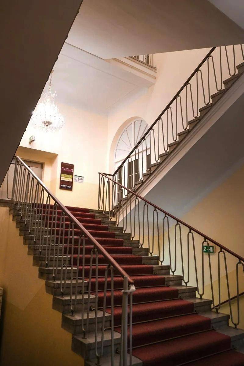 Elegantes Treppenhaus mit rotem Teppich, kunstvollen Geländern und einem großen Bogenfenster.