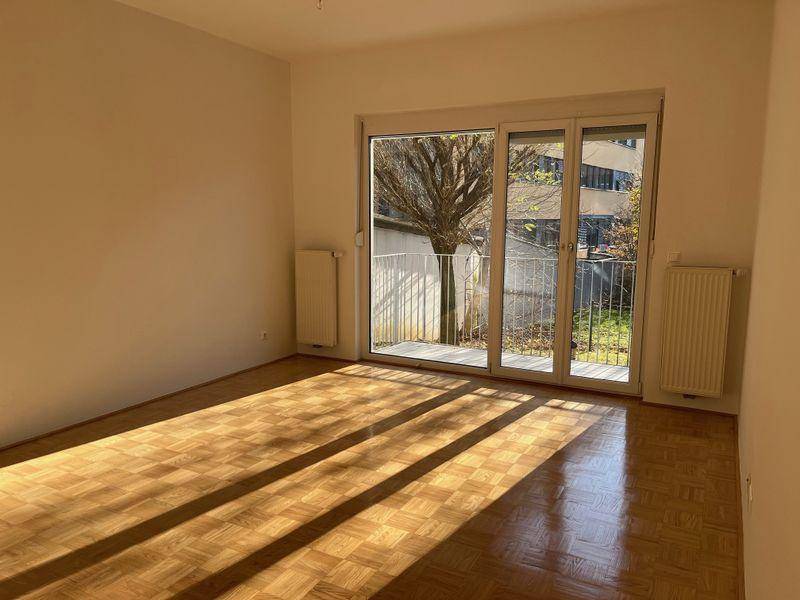 Lichtdurchflutetes Zimmer mit Parkettboden und großem Schiebefenster, das Zugang zu einem französischen Balkon bietet.