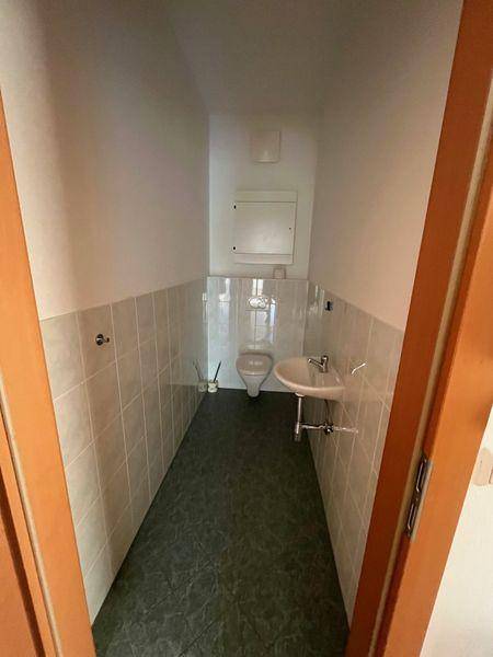 Kleines Gäste-WC mit Toilette, Waschbecken und halbhohen Fliesen an den Wänden, das eine Modernisierung benötigt.