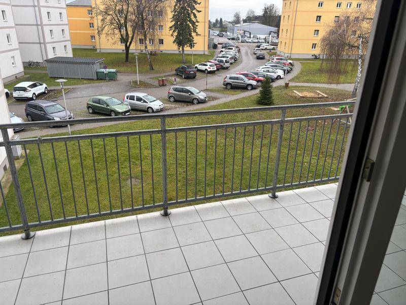 Balkon mit Fliesenboden und Blick auf den Innenhof mit Parkplätzen und Grünflächen.