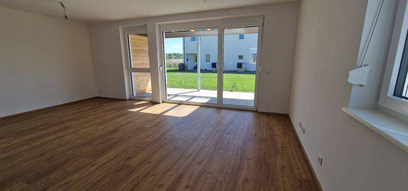 Geräumiges Wohnzimmer mit Laminatboden und großem Schiebefenster zum Garten.