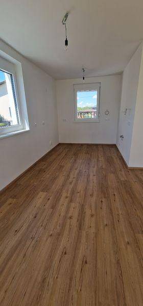 Heller Raum mit neuem Laminatboden und zwei Fenstern, bereit für individuelle Gestaltung.