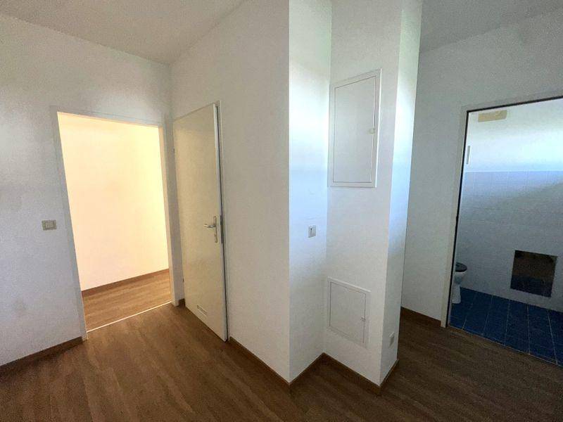 Flur mit Laminatboden und Blick in einen gefliesten Sanitärbereich.