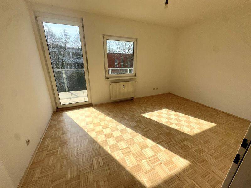 Sonniges Zimmer mit Fischgrätparkett und großer Balkontür.
