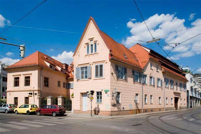 Gebäudeansicht von der Straßenecke mit traditioneller Architektur und hellen Fensterläden.