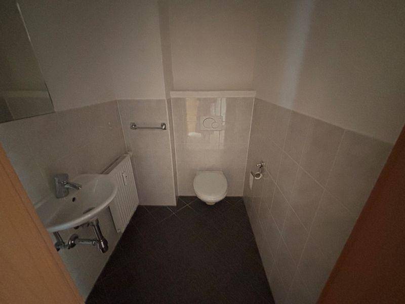 Kleines Gäste-WC mit Wand-WC, Waschbecken und hellen Fliesen an Wänden und Boden.