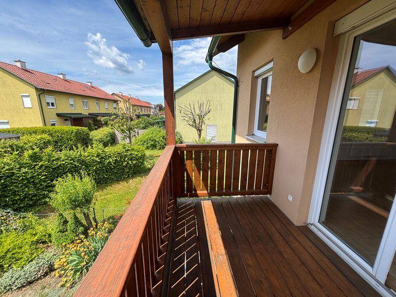 Geräumiger Holzbalkon mit Blick auf den grünen Garten und die umliegenden Häuser.