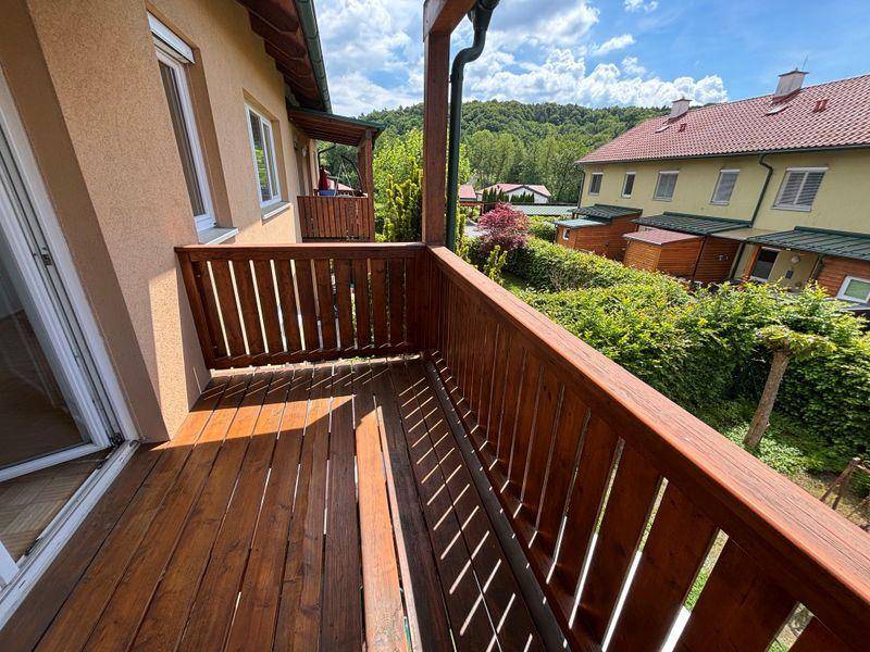 Sonniger Holzbalkon mit weitem Blick über grüne Gärten und bewaldete Hügel.