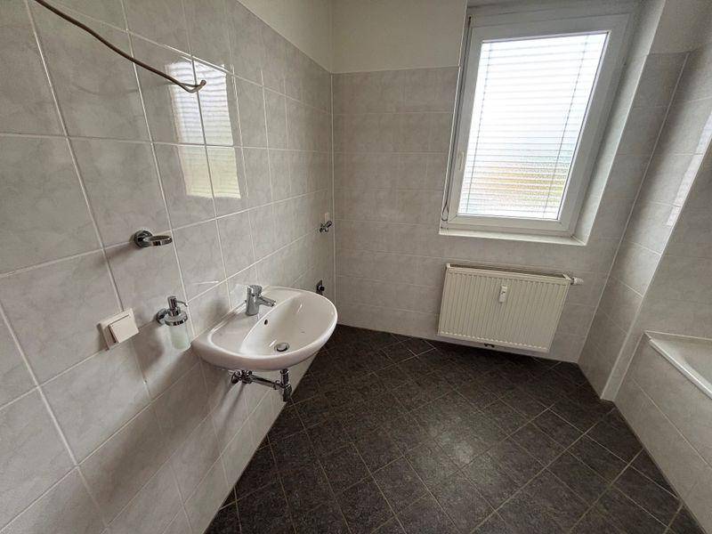 Helles Badezimmer mit Waschbecken, Fenster und grauen Fliesen, bietet viel Tageslicht.