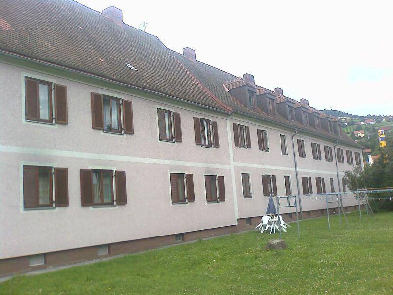 Längere Ansicht eines Wohngebäudes mit Satteldach, Fensterläden und einer grünen Rasenfläche davor.