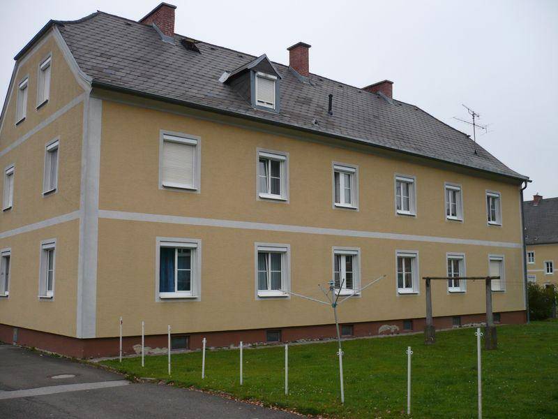 Seitenansicht eines Wohnhauses mit gelber Fassade, Schieferdach und Wäscheleine im Gartenbereich.