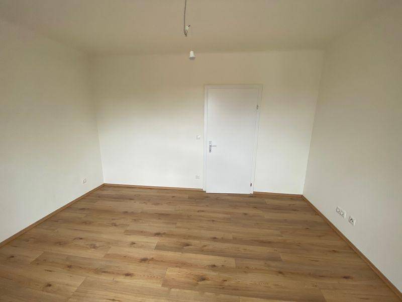 Leeres Zimmer mit hellem Laminatboden und frisch gestrichenen weißen Wänden, bereit zur Einrichtung.