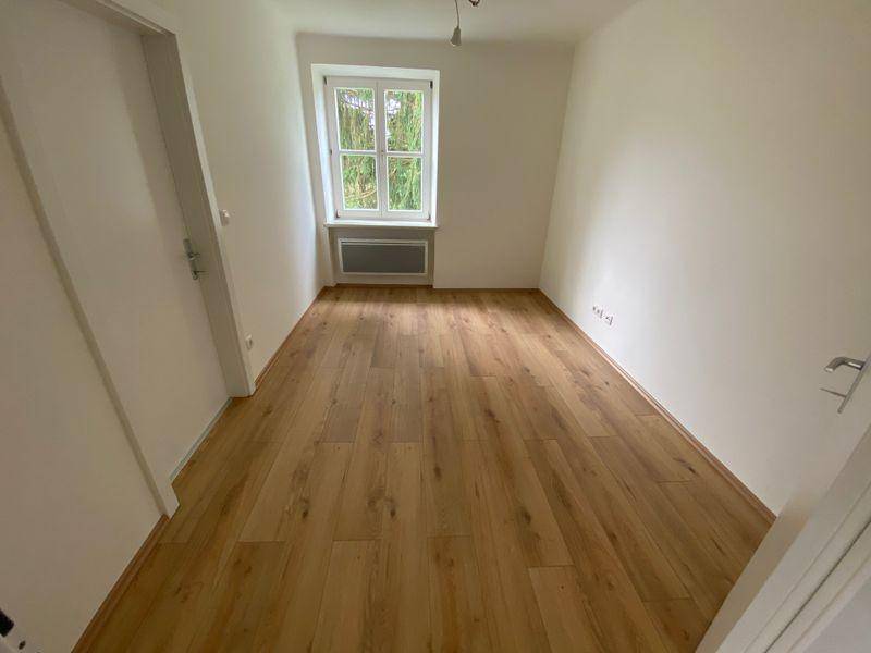 Helles Zimmer mit Laminatboden, einem Fenster mit Blick ins Grüne und einem Heizkörper.