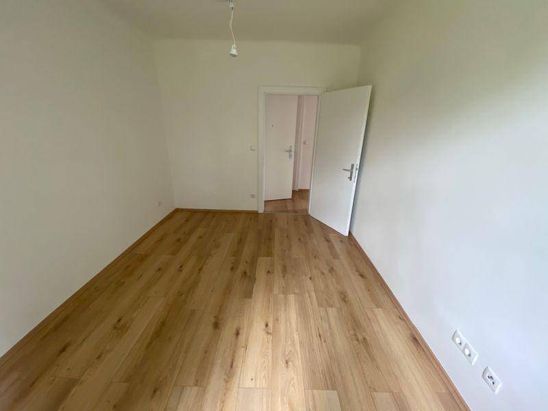 Leeres Zimmer mit Laminatboden und weiß gestrichenen Wänden, bereit für neue Bewohner.