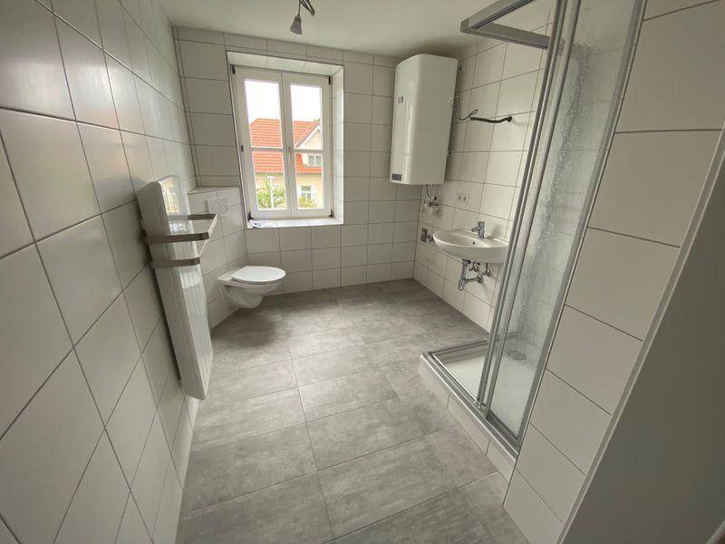 Modern gefliestes Badezimmer mit Dusche, WC, Waschbecken und Fenster für Tageslicht.