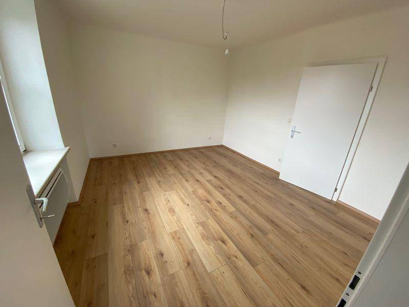 Helles Zimmer mit Laminatboden und weiß gestrichenen Wänden, ideal als Kinder- oder Gästezimmer.