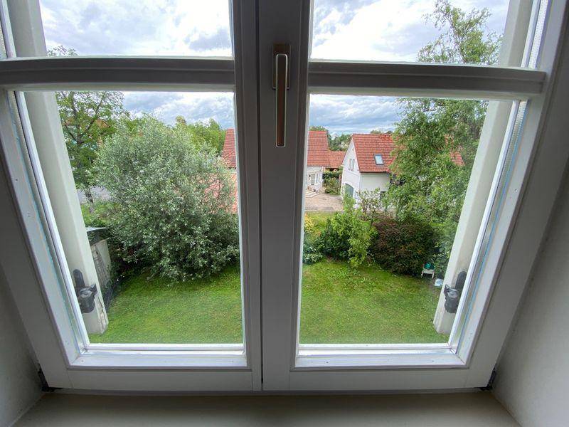 Fensterblick auf einen gepflegten Garten mit Rasenflächen und umliegenden Häusern.