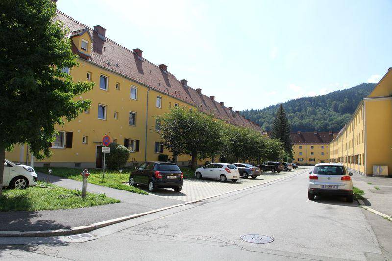 Reihen von gelben Wohngebäuden mit roten Ziegeldächern entlang einer Straße mit parkenden Autos.