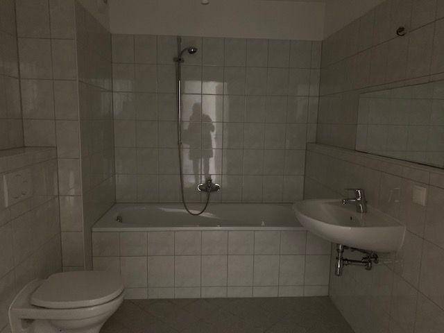 Gefliestes Badezimmer mit Badewanne, Duschvorrichtung, Toilette und Waschbecken in hellem Design.