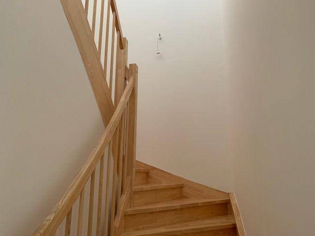 Helle Holztreppe mit Geländer, die in einem modernen Innenraum nach oben führt.