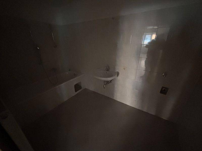 Dunkles Badezimmer mit Badewanne, Waschbecken und Fliesenboden, benötigt Renovierung.