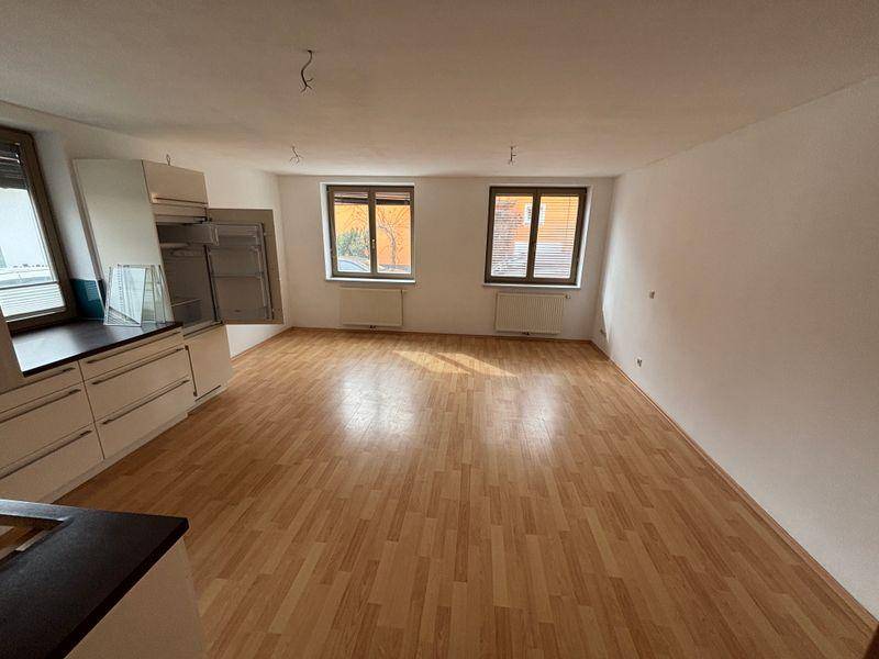 Offener Wohnbereich mit Laminatboden und Fenstern, teilweise als Küche vorbereitet.