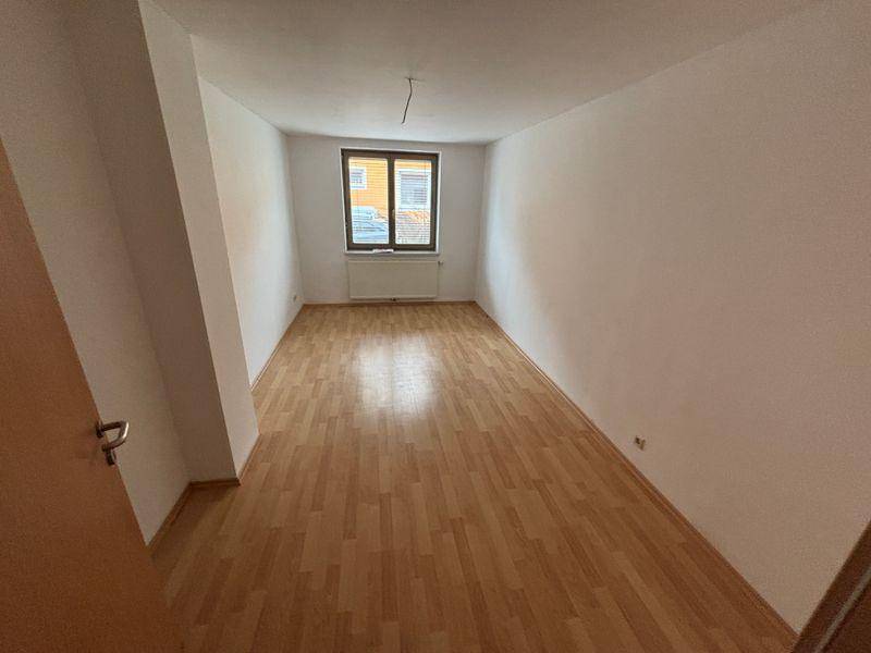 Leeres Schlafzimmer mit Laminatboden, weiß gestrichenen Wänden und einem Fenster.
