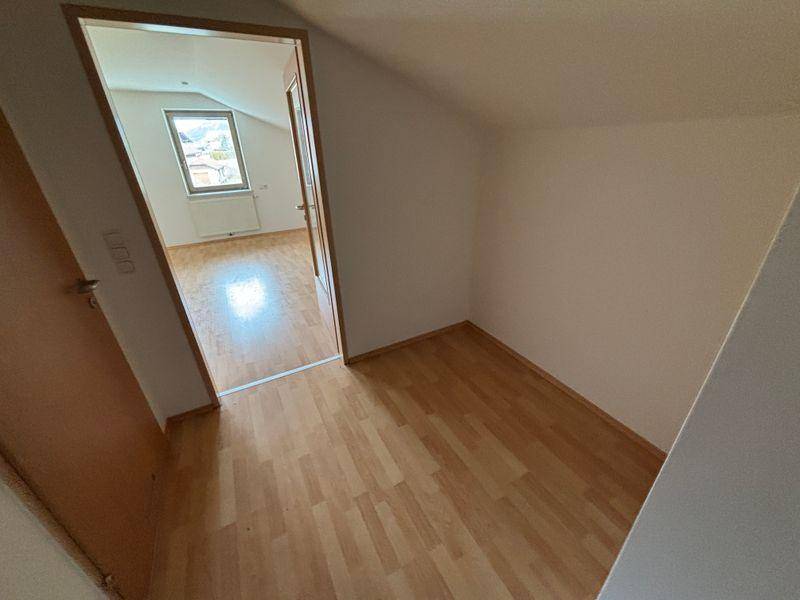 Kleiner Bereich mit Laminatboden und Zugang zu einem hellen Zimmer mit Dachschräge und Fenster.