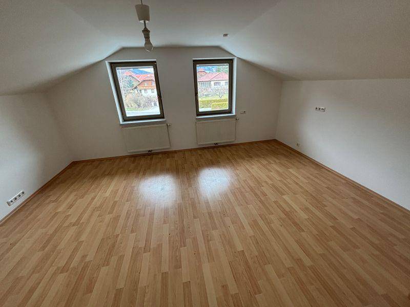 Helles Dachgeschosszimmer mit Laminatboden und zwei Fenstern, die einen Blick ins Grüne bieten.