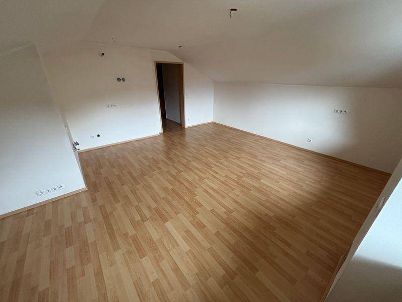 Weiterer Blick in das helle Dachgeschosszimmer mit Laminatboden und Zugang zu einem anderen Raum.