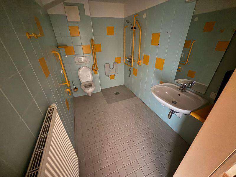 Barrierefreies Badezimmer mit blauen und gelben Fliesen, Haltegriffen und ebenerdiger Dusche.