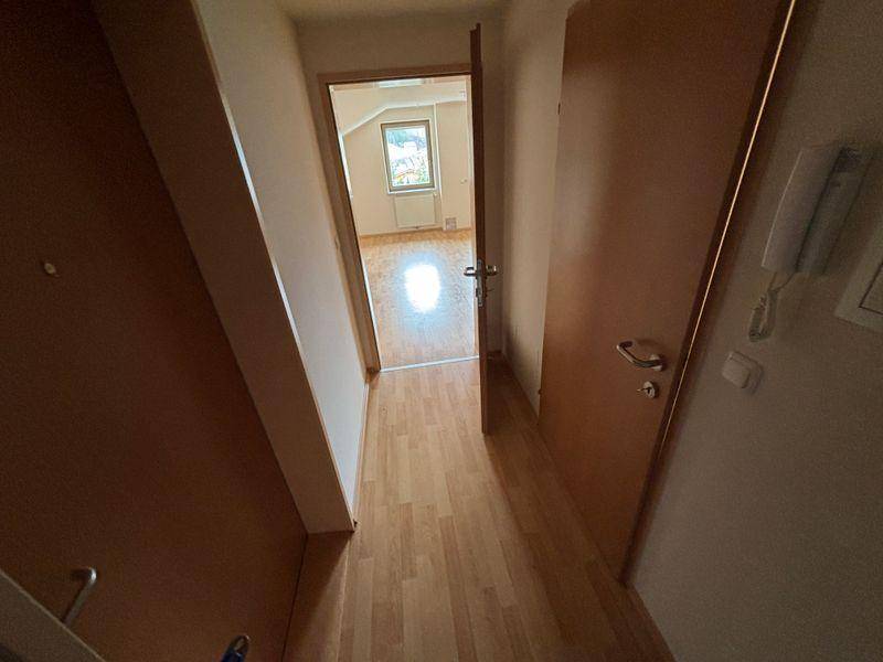 Heller Flur mit Laminatboden, der zu einem weiteren Zimmer mit Fenster und Tageslicht führt.