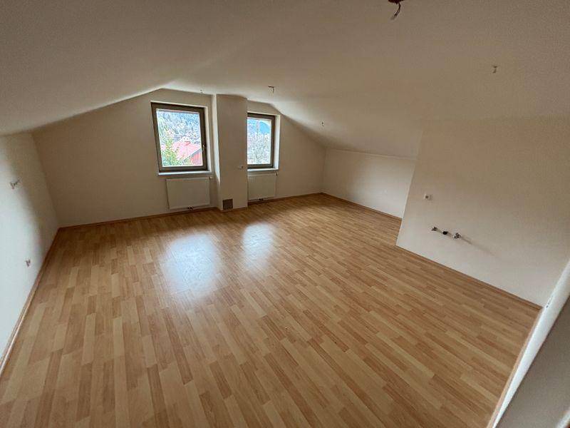 Geräumiges Zimmer im Dachgeschoss mit Laminatboden, schrägen Wänden und zwei Fenstern mit Ausblick.