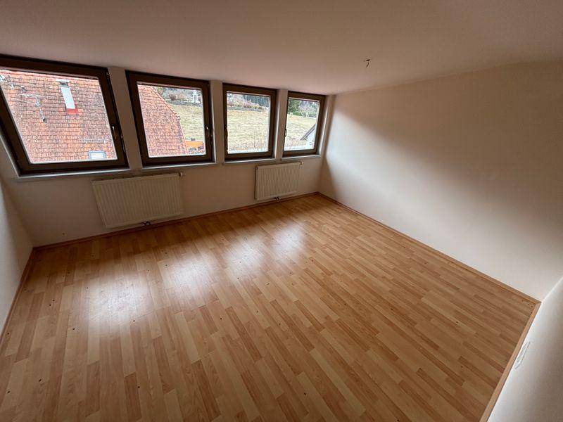 Helles Zimmer mit Laminatboden und mehreren Fenstern, die einen weiten Blick ins Grüne bieten.