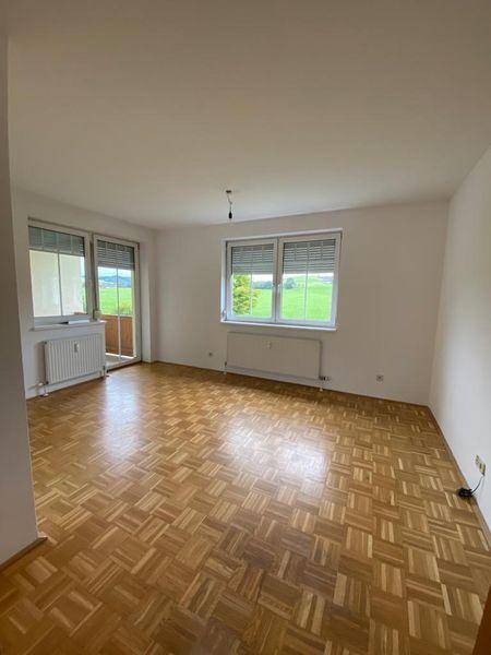 Geräumiger, heller Wohnraum mit Parkettboden und Zugang zu einem Balkon.