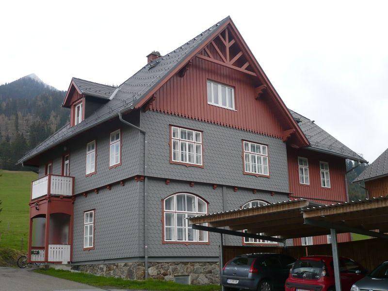 Traditionelles Haus mit Balkon und Carport, umgeben von grüner Landschaft.