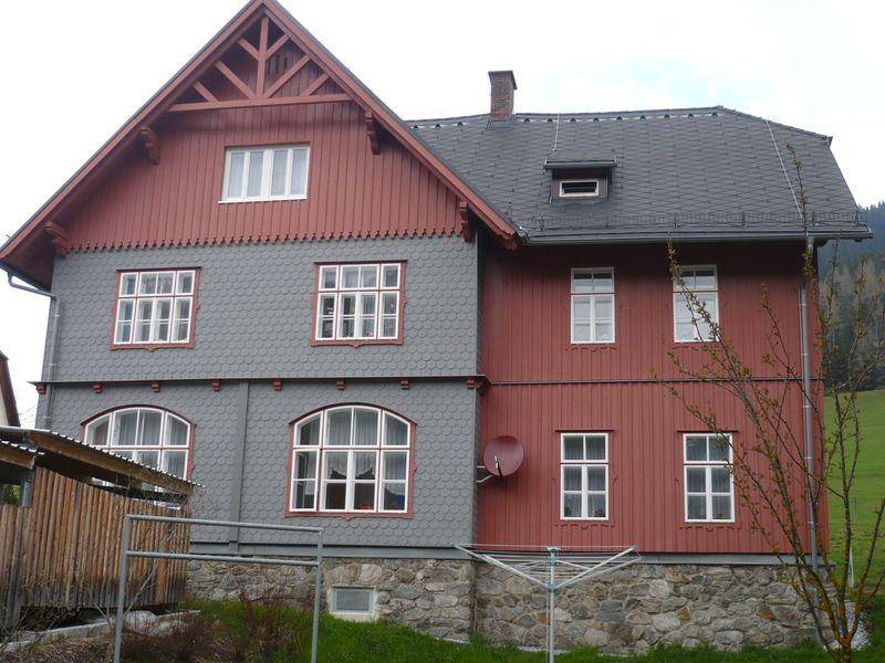 Traditionelles Haus mit roter Holzverkleidung und grauen Schindeln in ländlicher Umgebung.