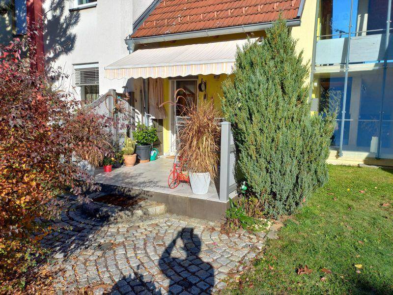 Gemütliche Terrasse mit Markise und Pflanzen, umgeben von Herbstlaub und Grünflächen.