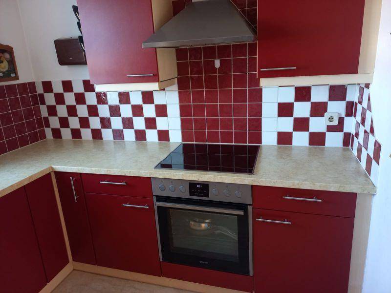 Moderne Küche mit roten Schränken, Induktionskochfeld und Backofen, gefliestem Spritzschutz.