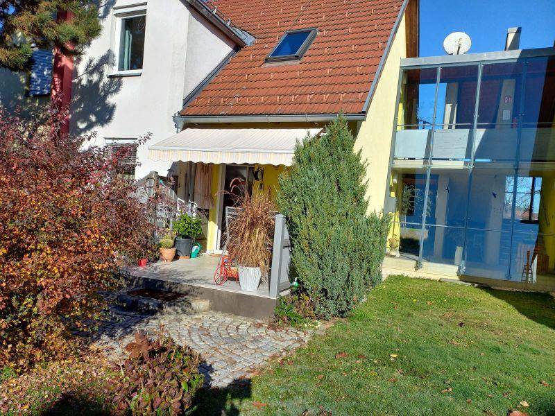 Sonniger Außenbereich mit Terrasse, Markise und einer modernen Glaserweiterung des Hauses.