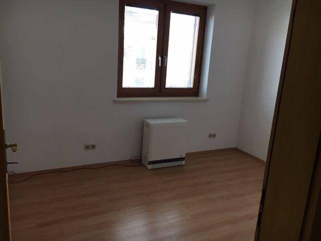Leeres Zimmer mit Laminatboden und einem großen Fenster, das für gute Belichtung sorgt.