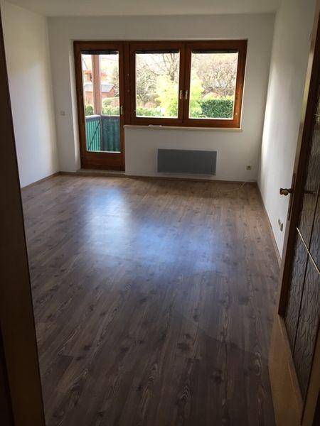 Helles Wohnzimmer mit Laminatboden und Zugang zu einem Balkon mit Blick ins Grüne.